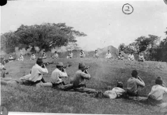 Soldados japoneses atirando em prisioneiros indiano da etnia Sikh, que estão sentados com os olhos vendados em um semi-círculo a cerca de 20 metros de distância. Fotografia encontrada entre os registros japoneses quando as tropas britânicas reocuparam Cingapura.